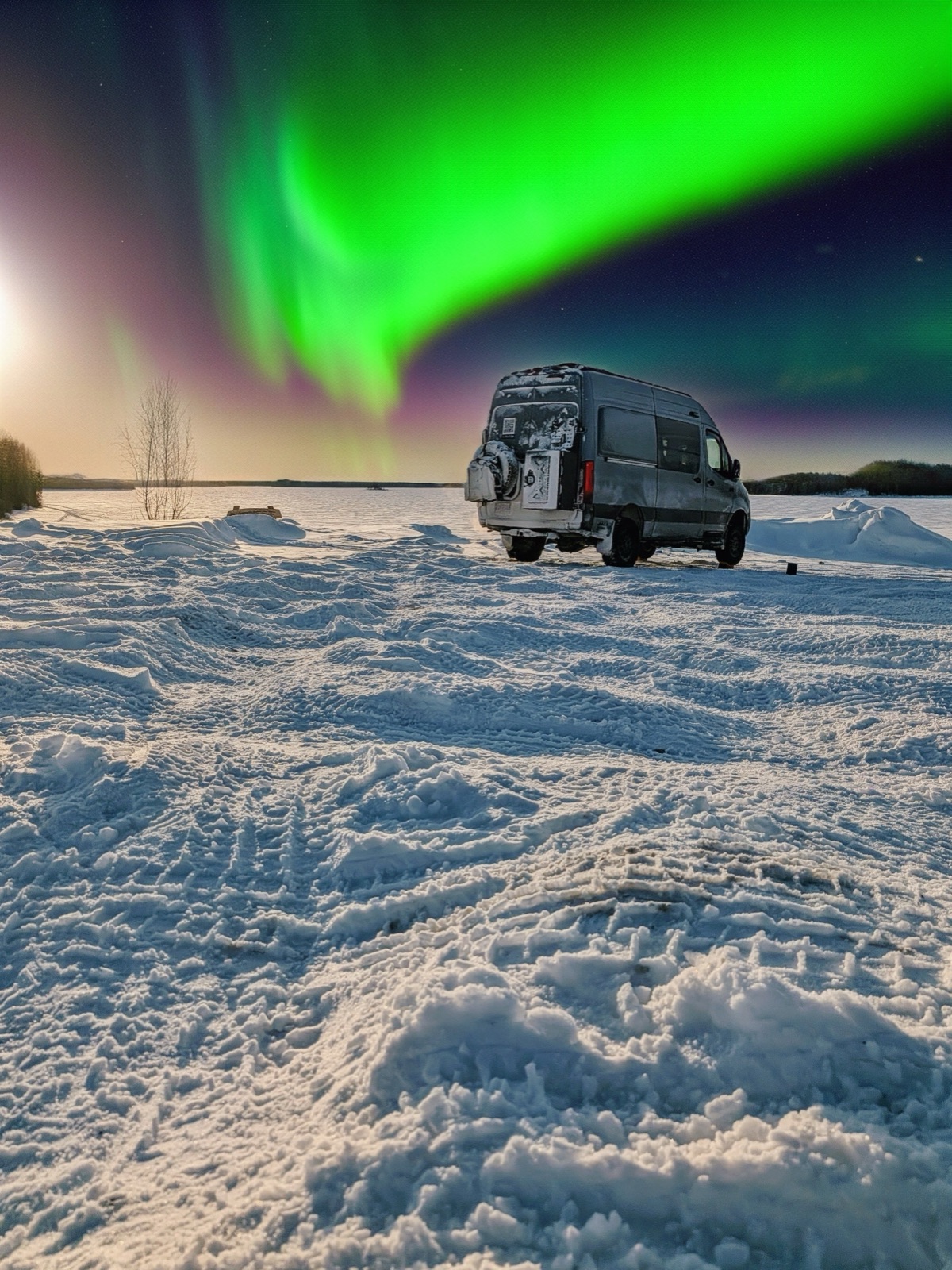 The van parked on a frozen lake beneath the green northern lights.