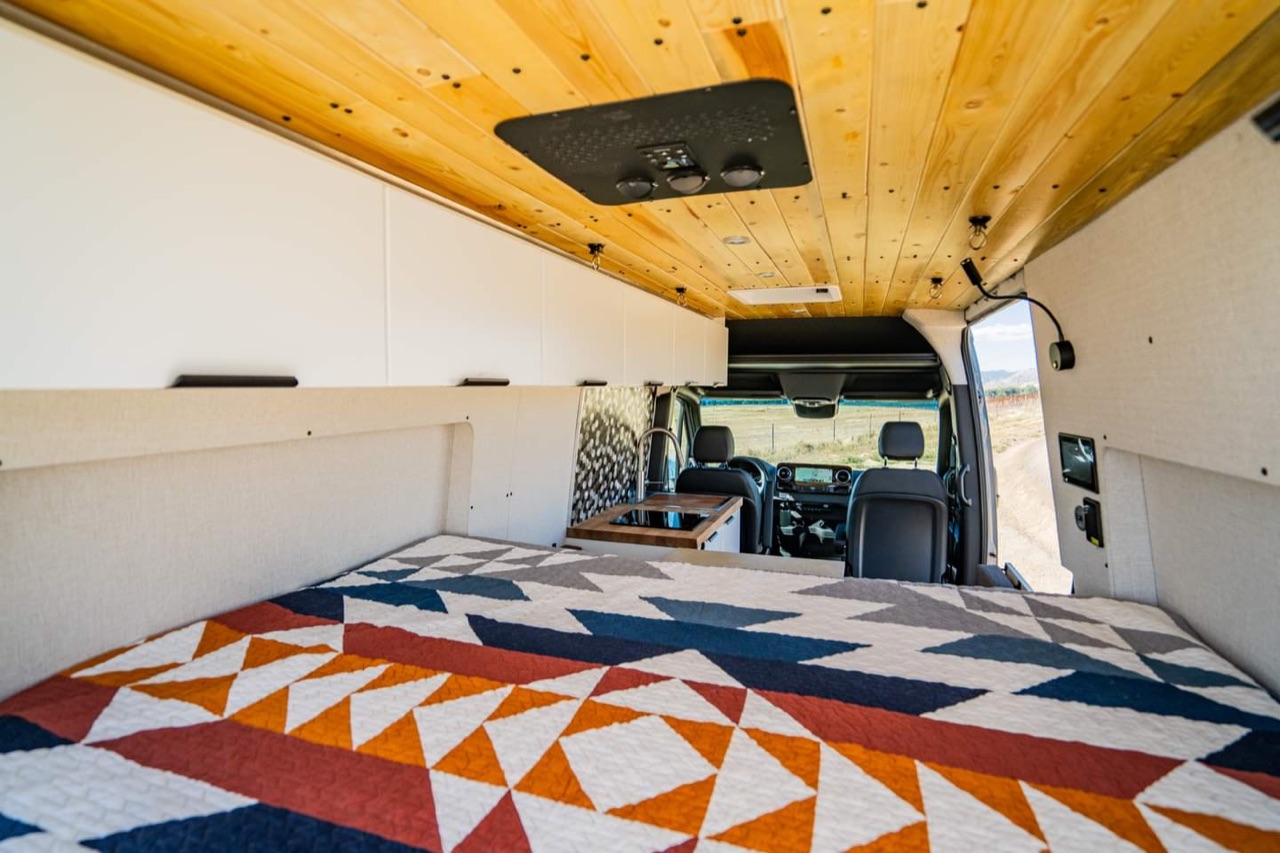 The van galley — wood ceiling, kitchen counter, and patterned rug.